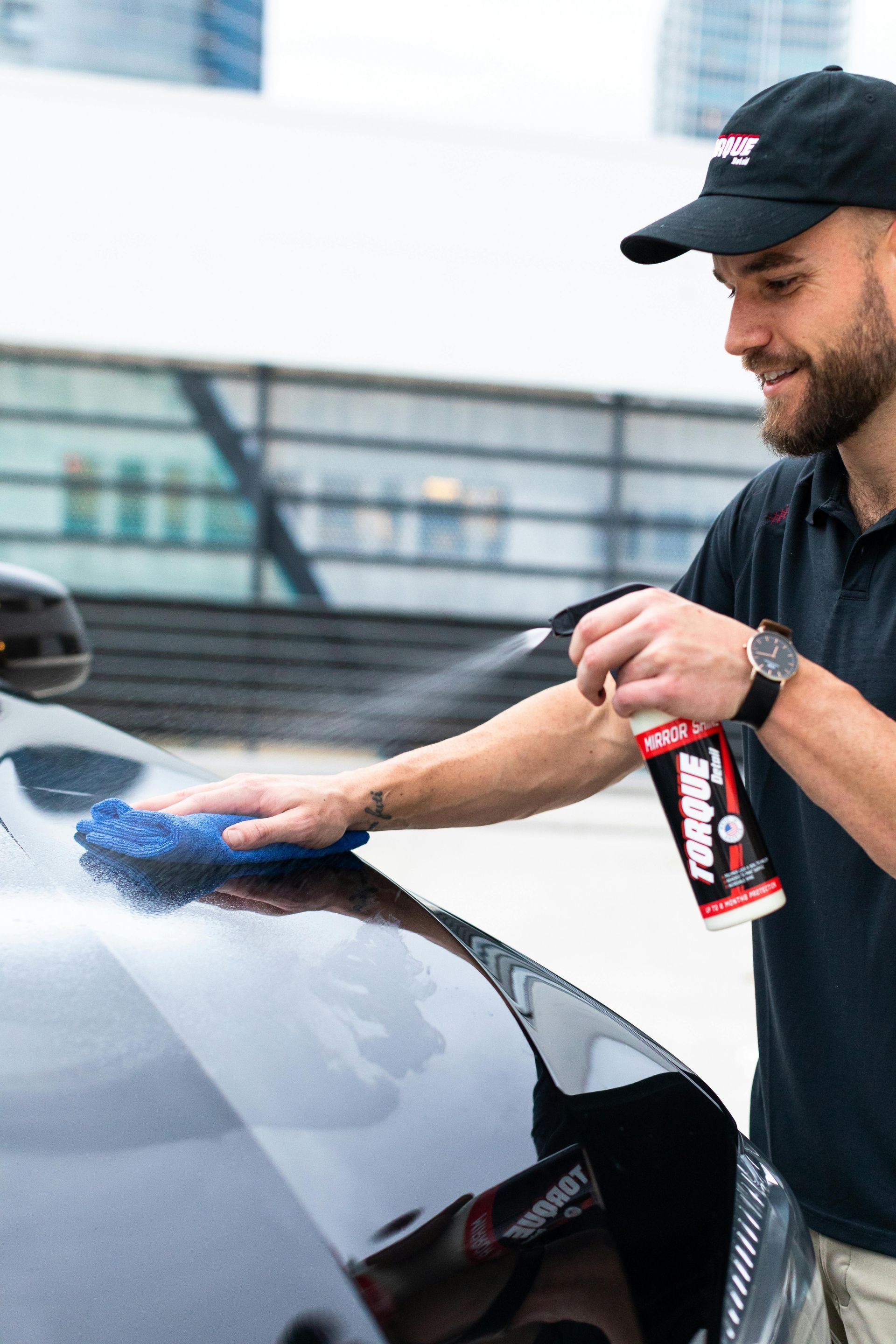 A man is cleaning the hood of a car with a cloth.