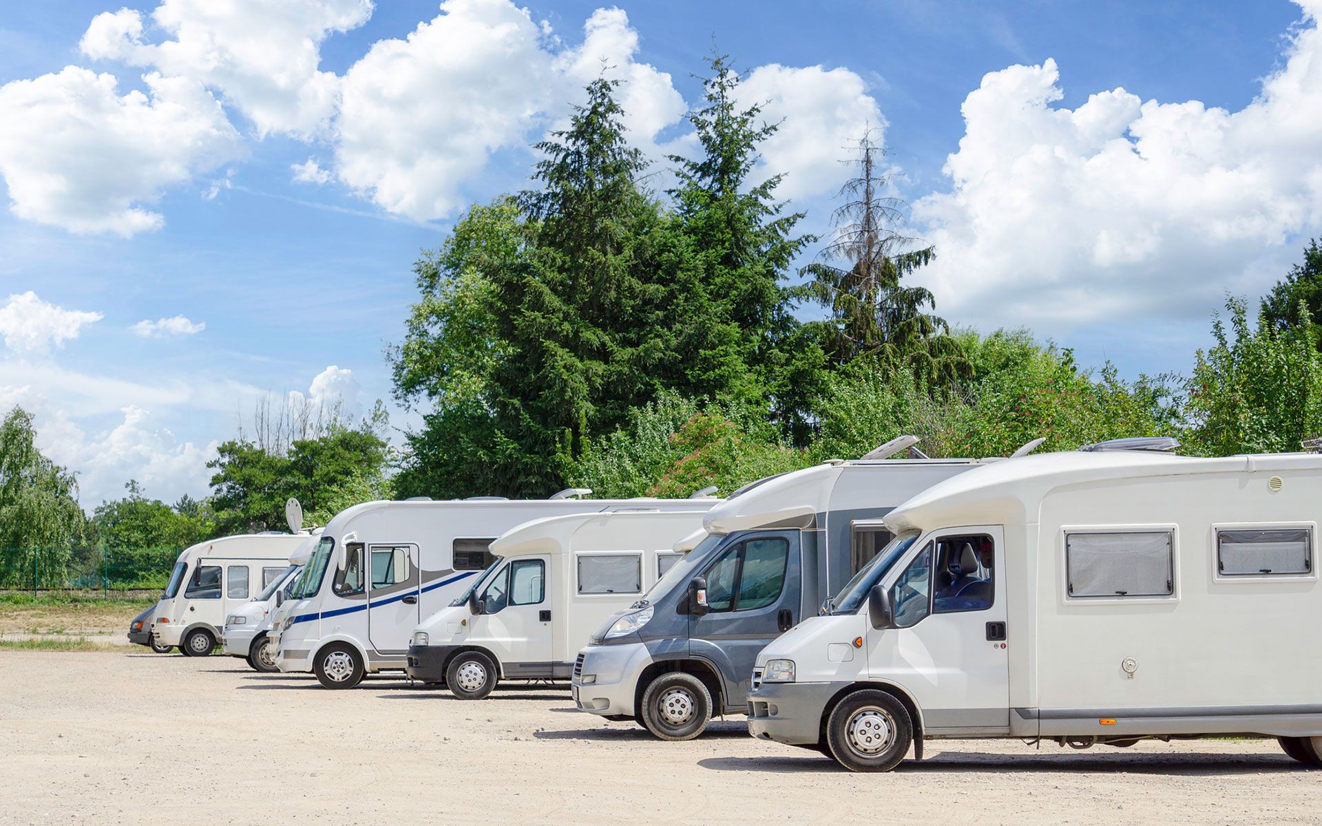 A row of rvs are parked in a gravel lot.