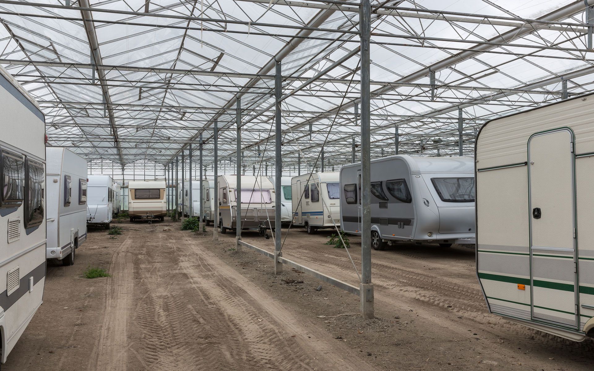 A row of caravans are parked under a greenhouse.