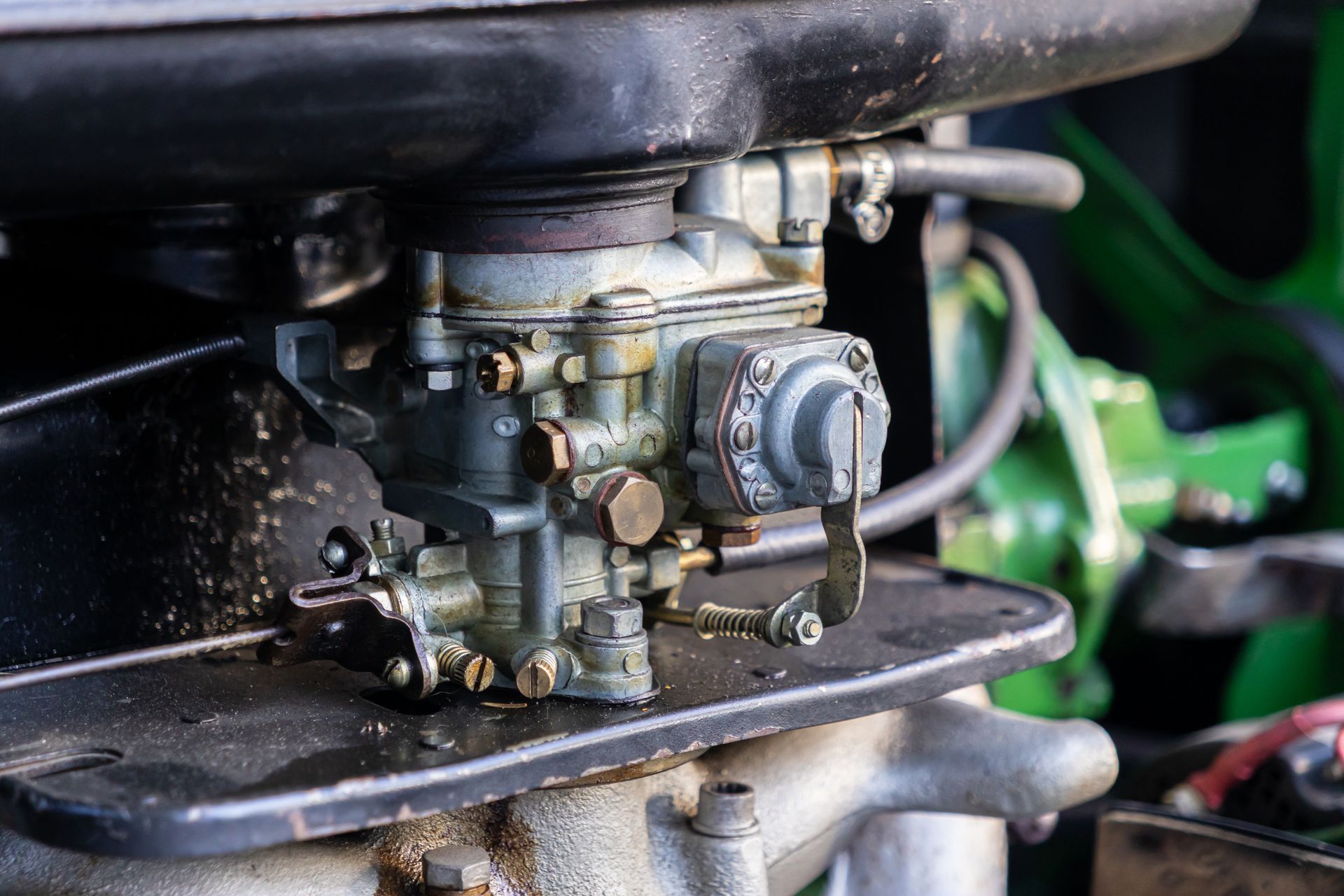 A close-up of a vintage engine carburetor mounted on a black metal plate with attached hoses and mechanical linkages.