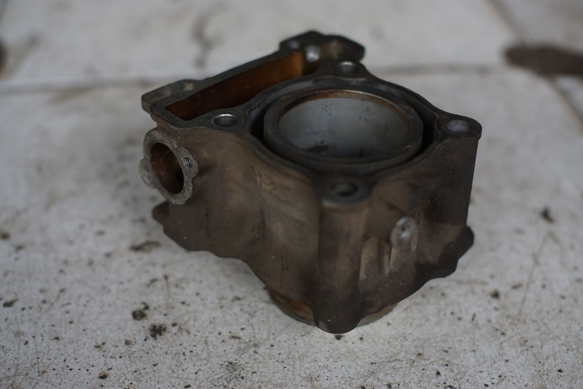 A used, dirty motorcycle engine cylinder block sitting on a stained concrete surface.