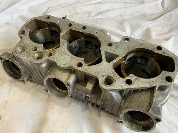 A weathered, three-cylinder engine block component made of cast metal, shown from an elevated, angled perspective.