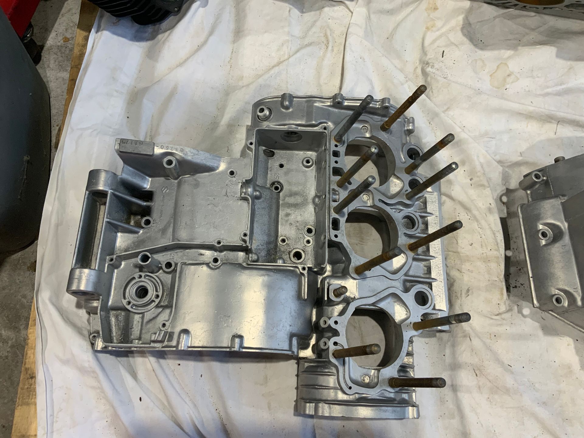 A disassembled, silver-colored motorcycle engine crankcase with exposed cylinder bores and protruding mounting studs.