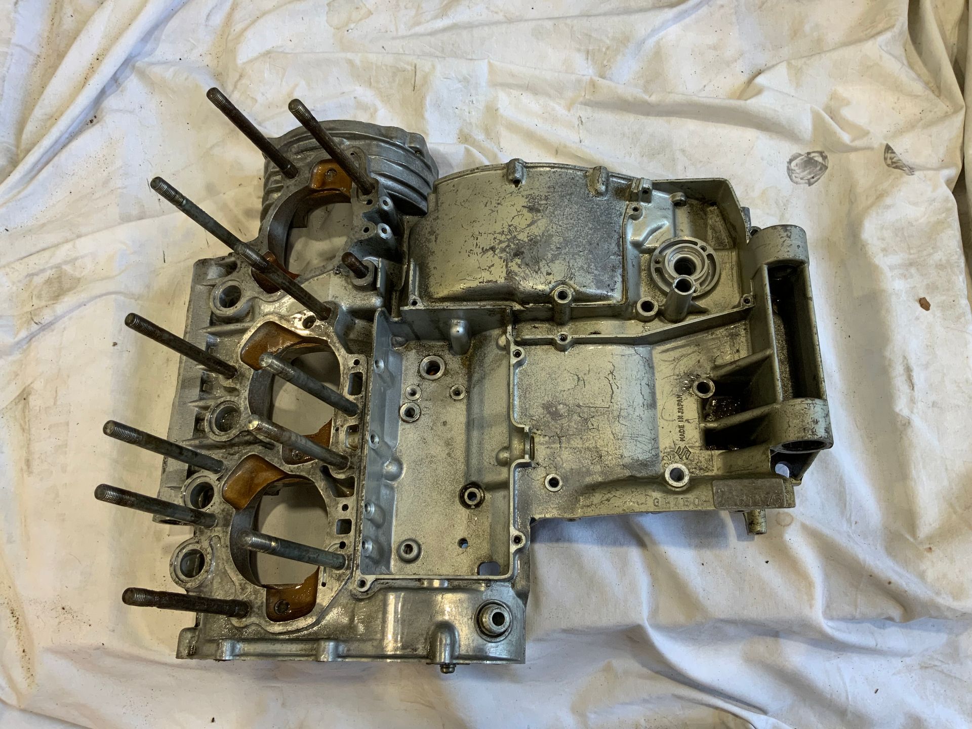 A disassembled aluminum motorcycle engine crankcase with vertical cylinder studs, resting on a white cloth surface.