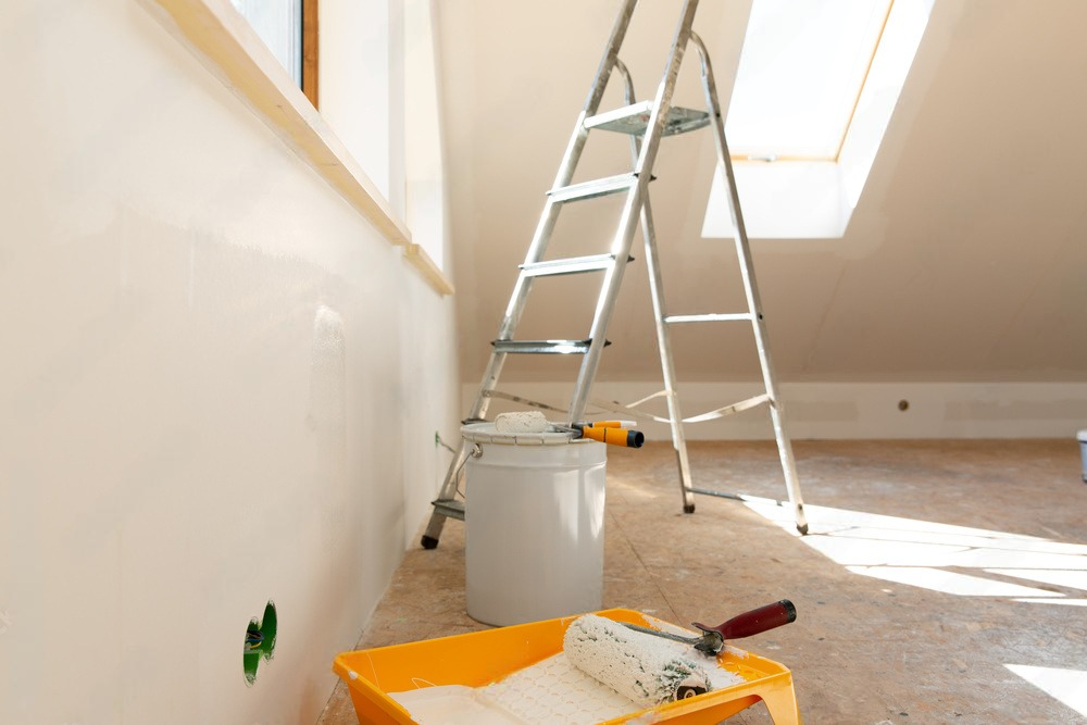 a bucket of paint sits next to a roller and a ladder