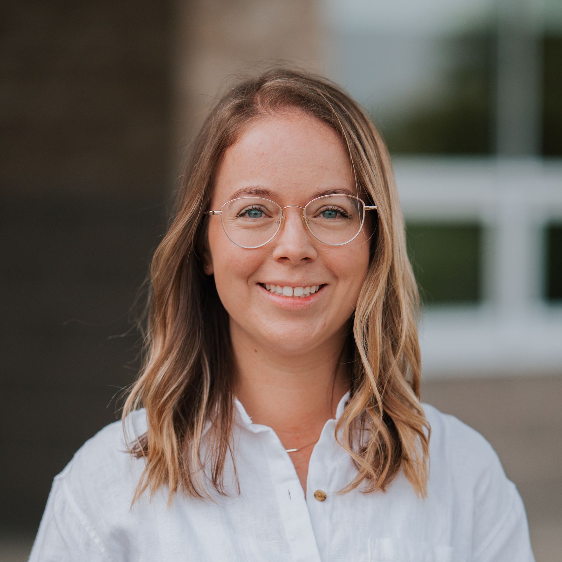 Woman with glasses smiles at camera, wearing a white button-down shirt.