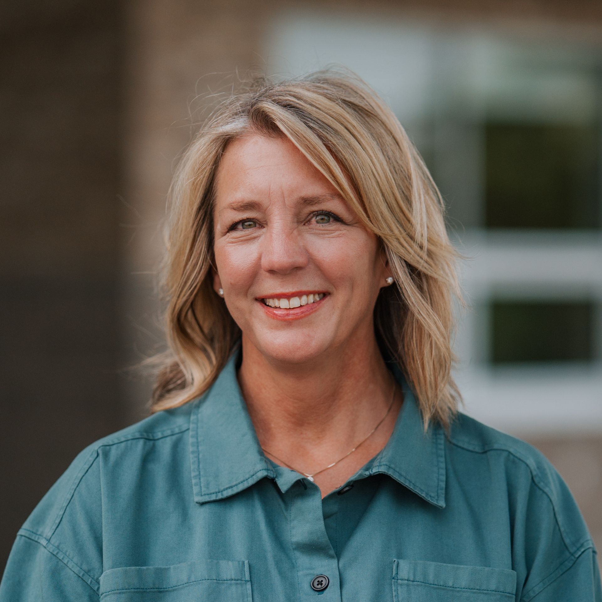 Woman with blonde hair wearing a teal shirt smiling in front of a building.