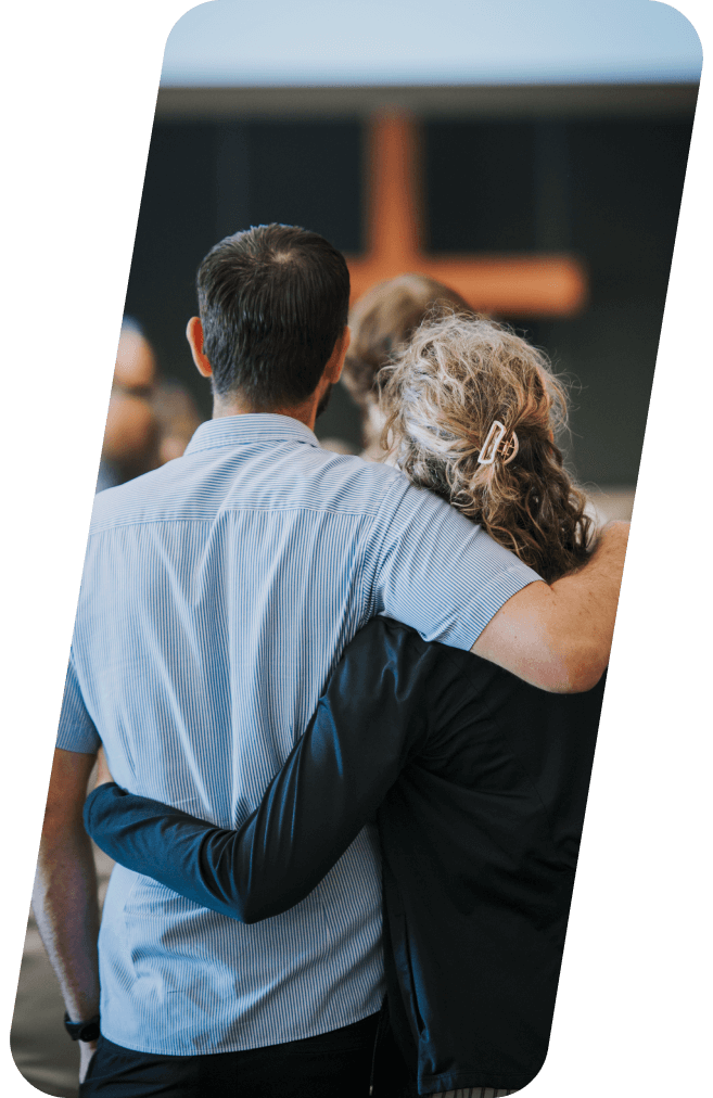 Couple with arms around each other, looking toward a cross in a church.