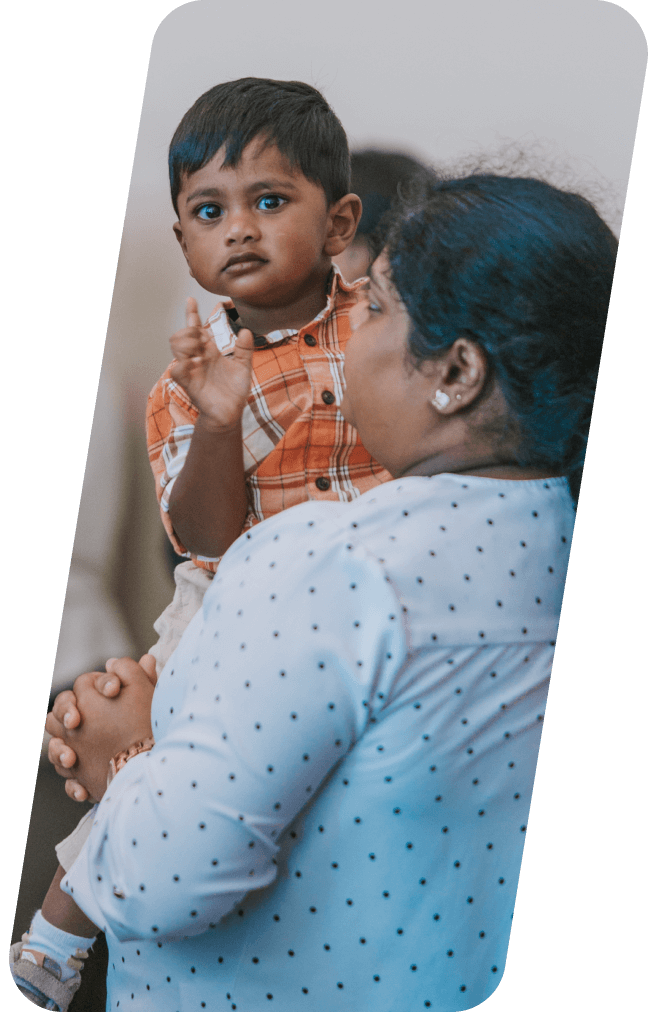 Woman holding a child; the child waves and looks toward the camera.