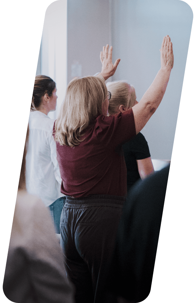 Woman with arms raised in a group of people, possibly in a class or workshop.