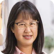 Woman with glasses, short black hair, wearing a pink shirt, smiling indoors.