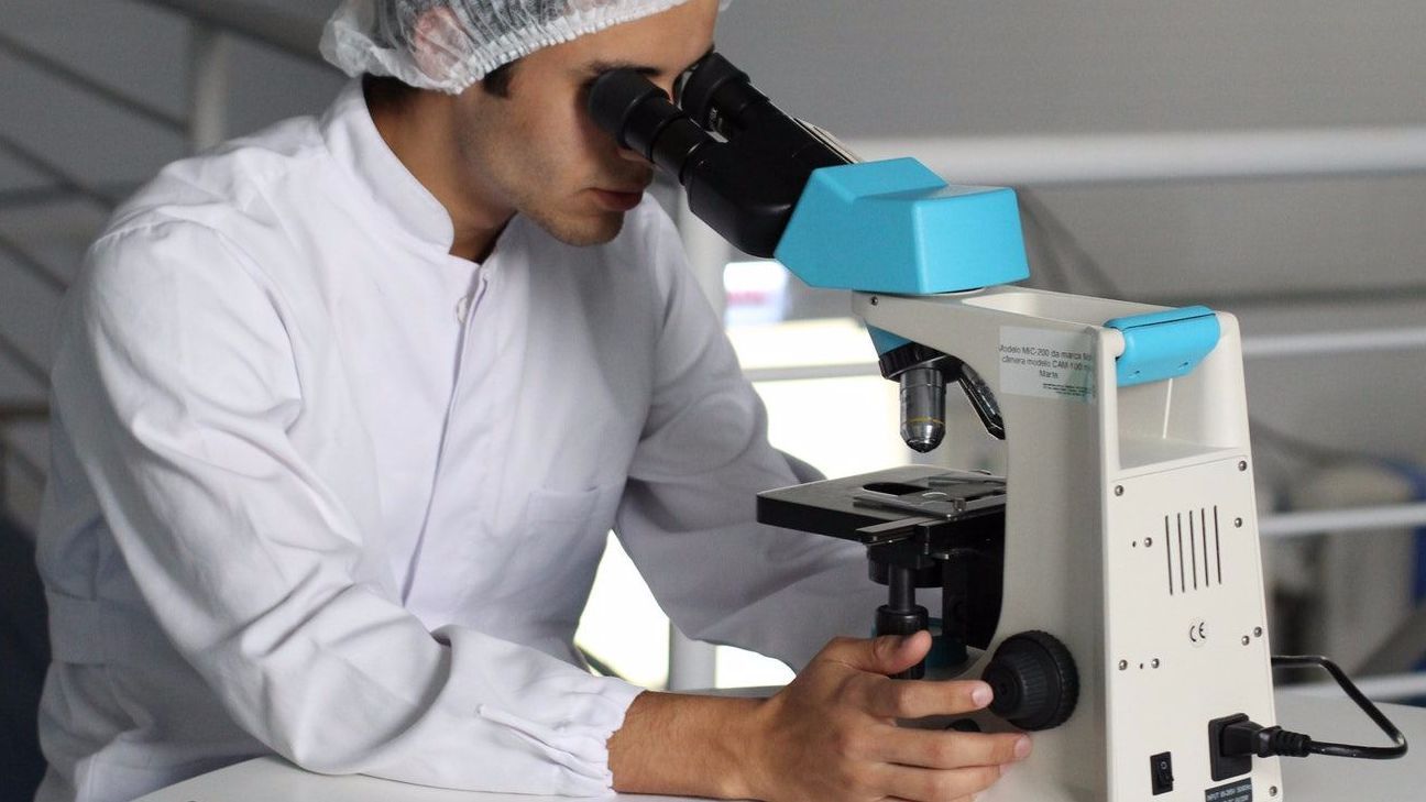 A man in a lab coat is looking through a microscope.