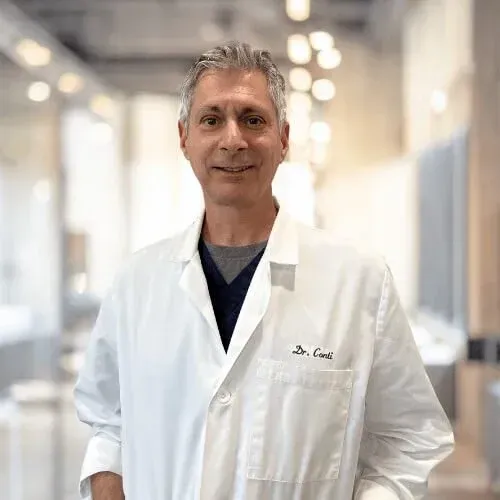 A smiling doctor in a lab coat with a stethoscope around his neck.