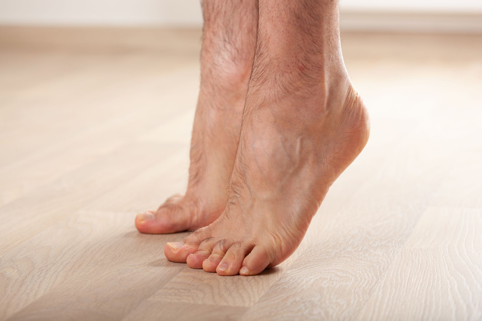 Bare feet on tiptoes, indoors, on a wooden floor.