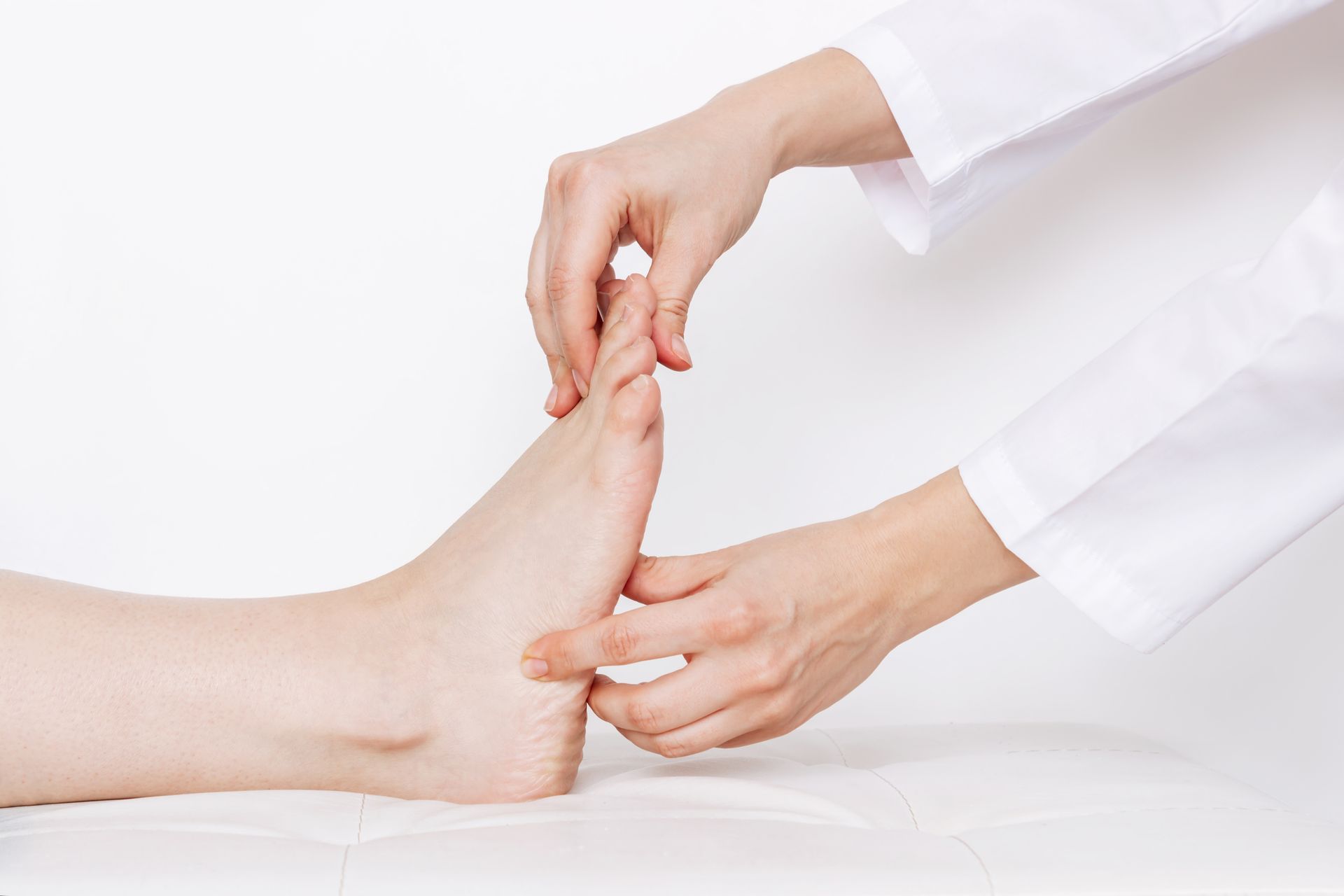 Doctor examining a patient's foot on a white table. They are wearing white coats.