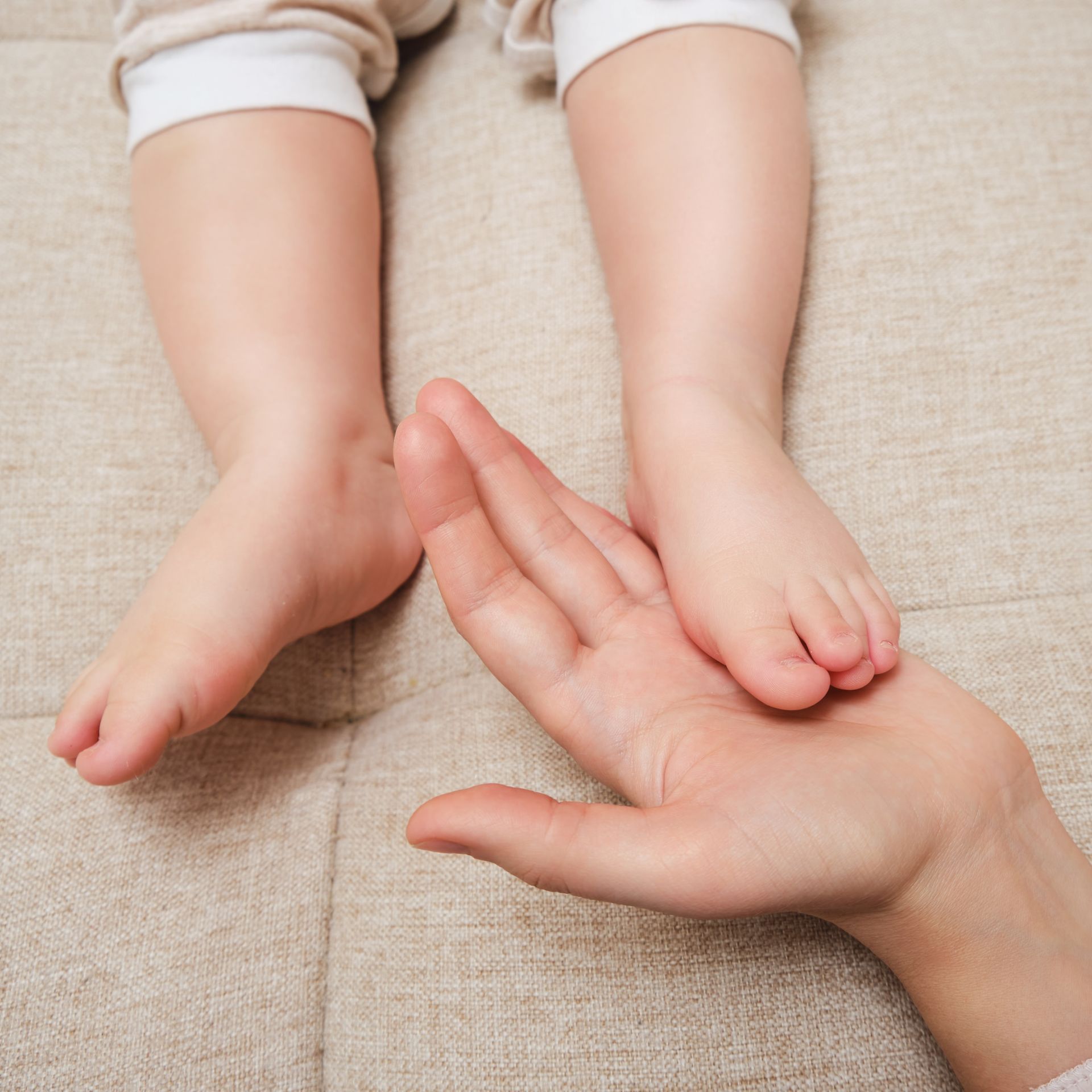 Baby's foot resting in an adult's open hand on a light-colored surface.