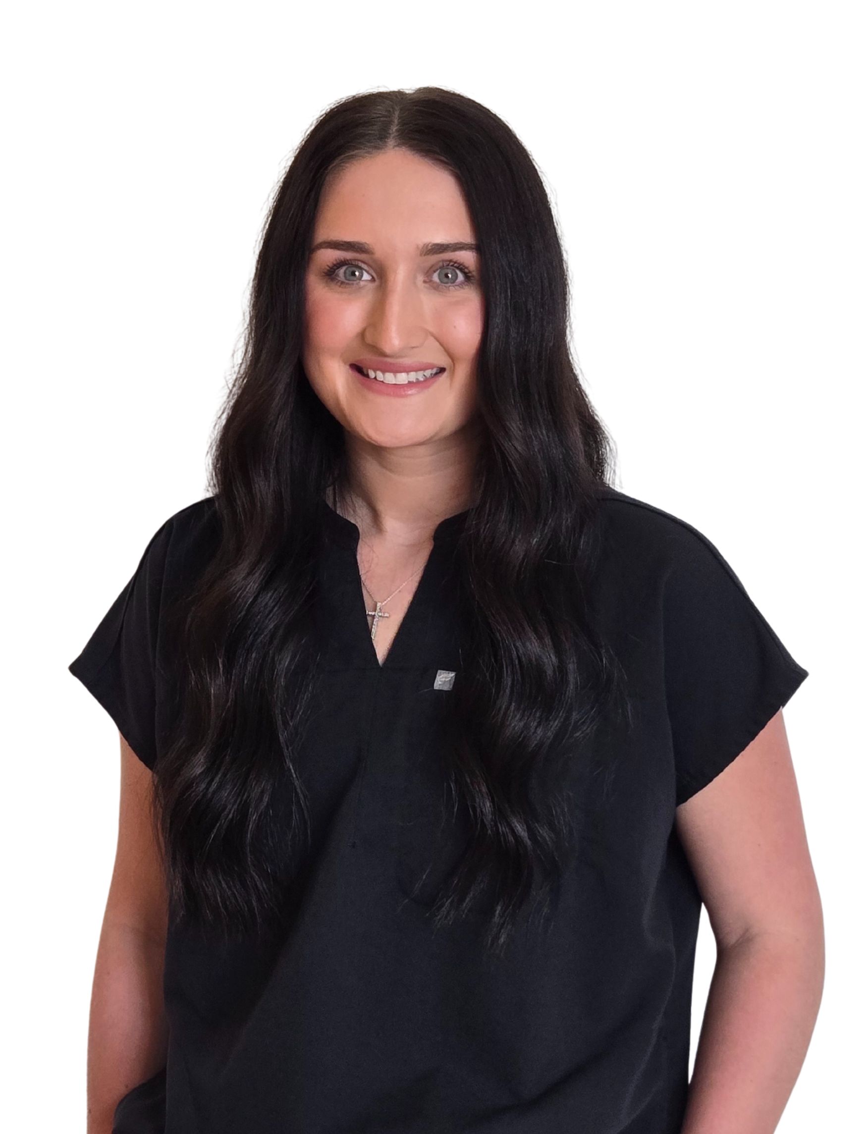 Woman smiling in black scrubs standing against white backdrop. 