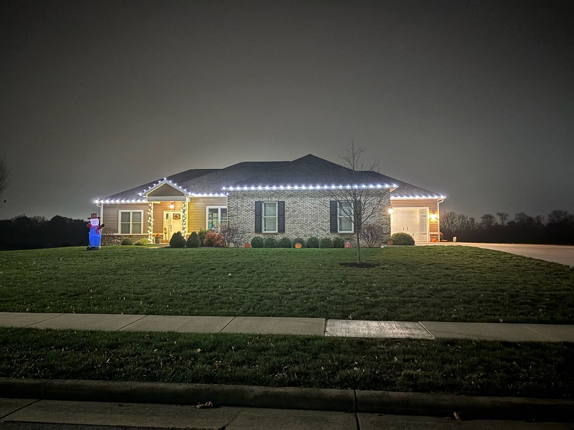 House with white Christmas lights on roofline, front lawn at night.
