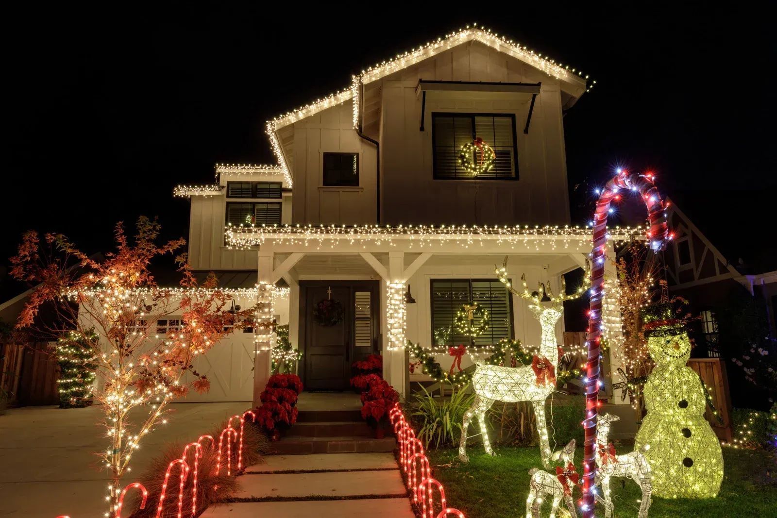 House lit up with white Christmas lights and decorations, including reindeer and a snowman.