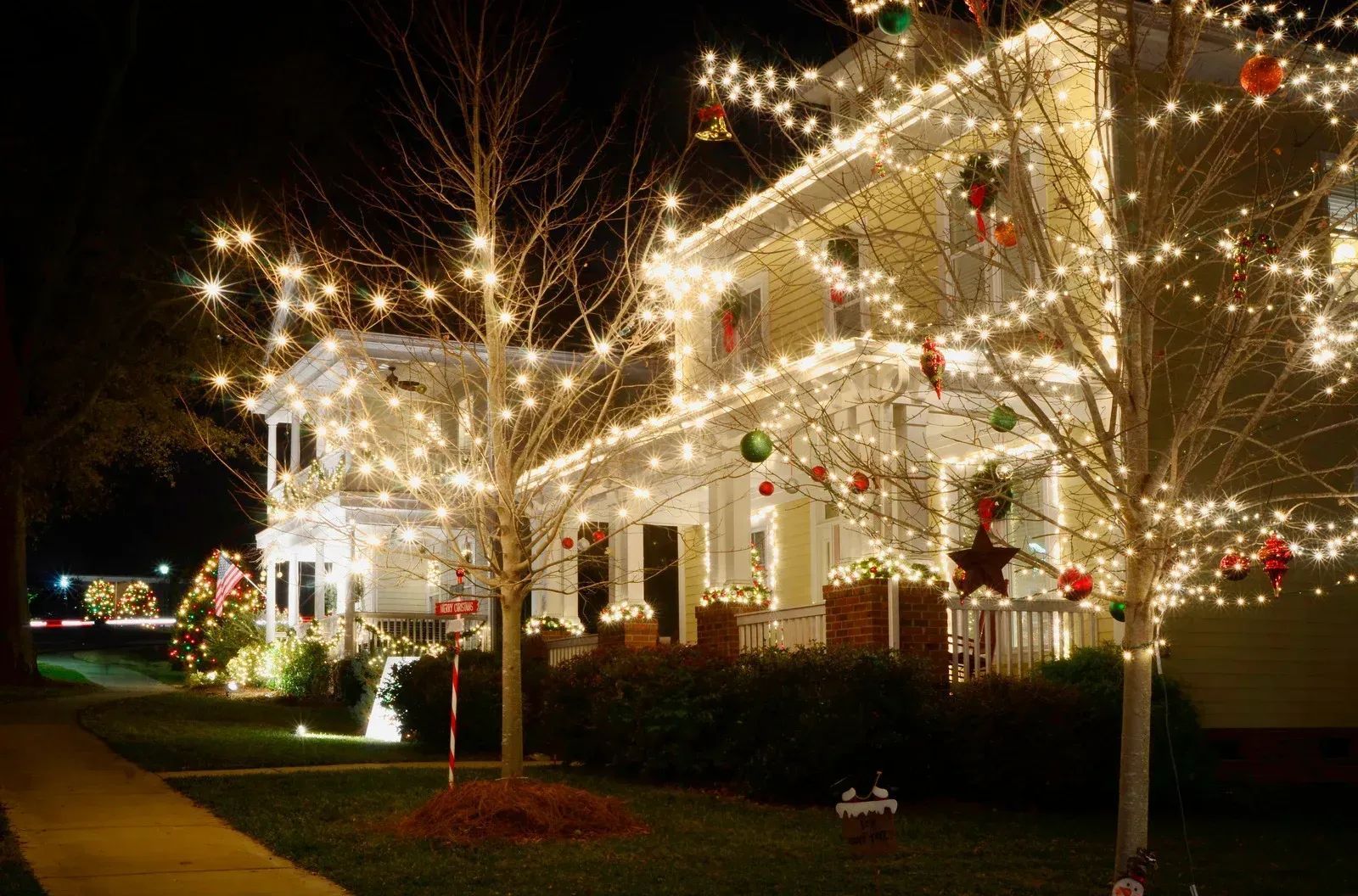 House decorated with bright white Christmas lights, garlands, and ornaments at night.