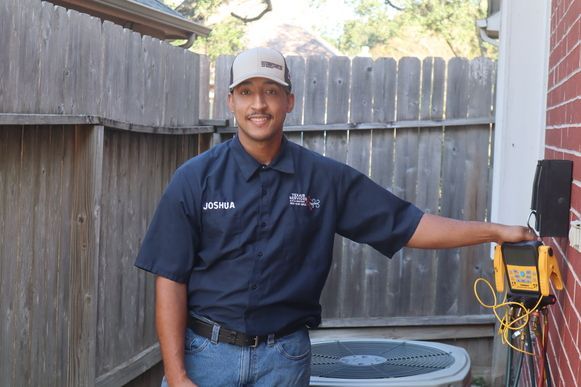 Man in blue work shirt holding a device against a brick wall.  Outdoor setting, near an air conditioning unit.