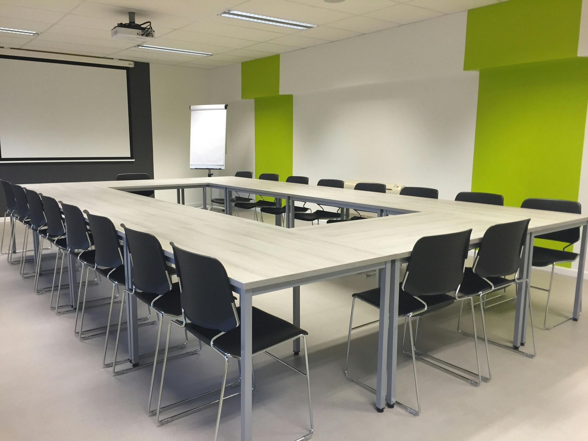 A U-shaped conference table with black chairs in a brightly lit room featuring white walls and lime green accents.
