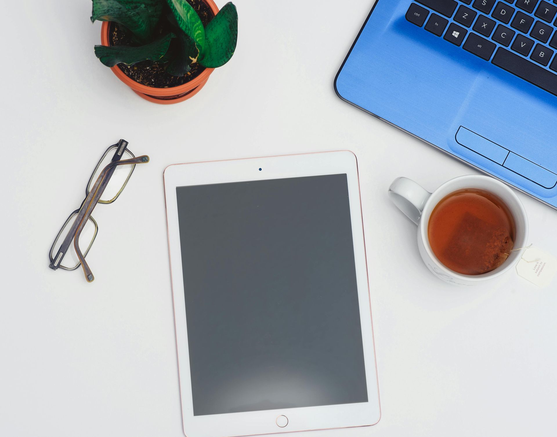 A tablet is on a table next to a laptop and a cup of tea