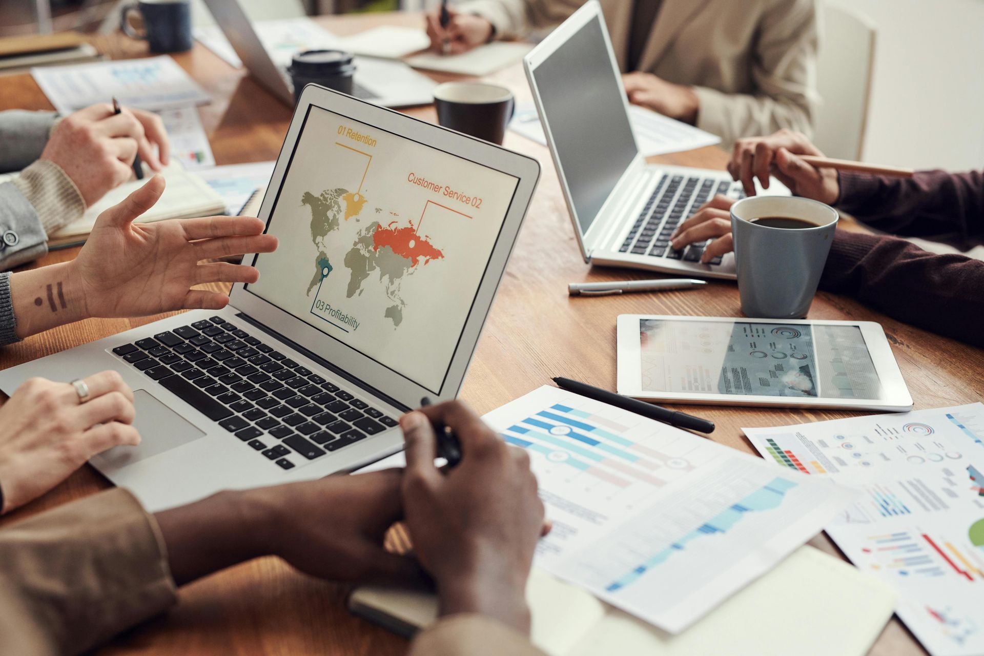 People at a table in a business meeting, with laptops, papers, and a world map diagram on a screen.