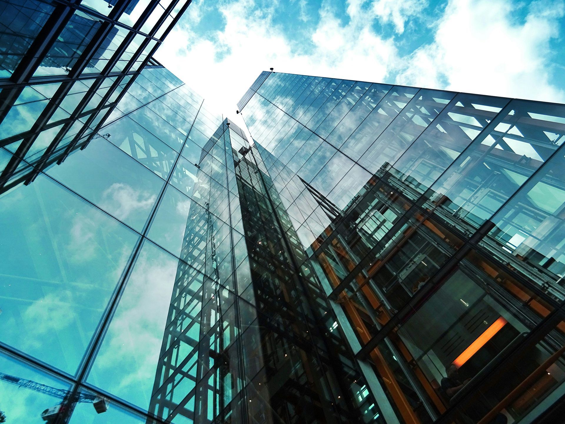 A low-angle view looking up at modern glass skyscrapers against a blue, cloudy sky.