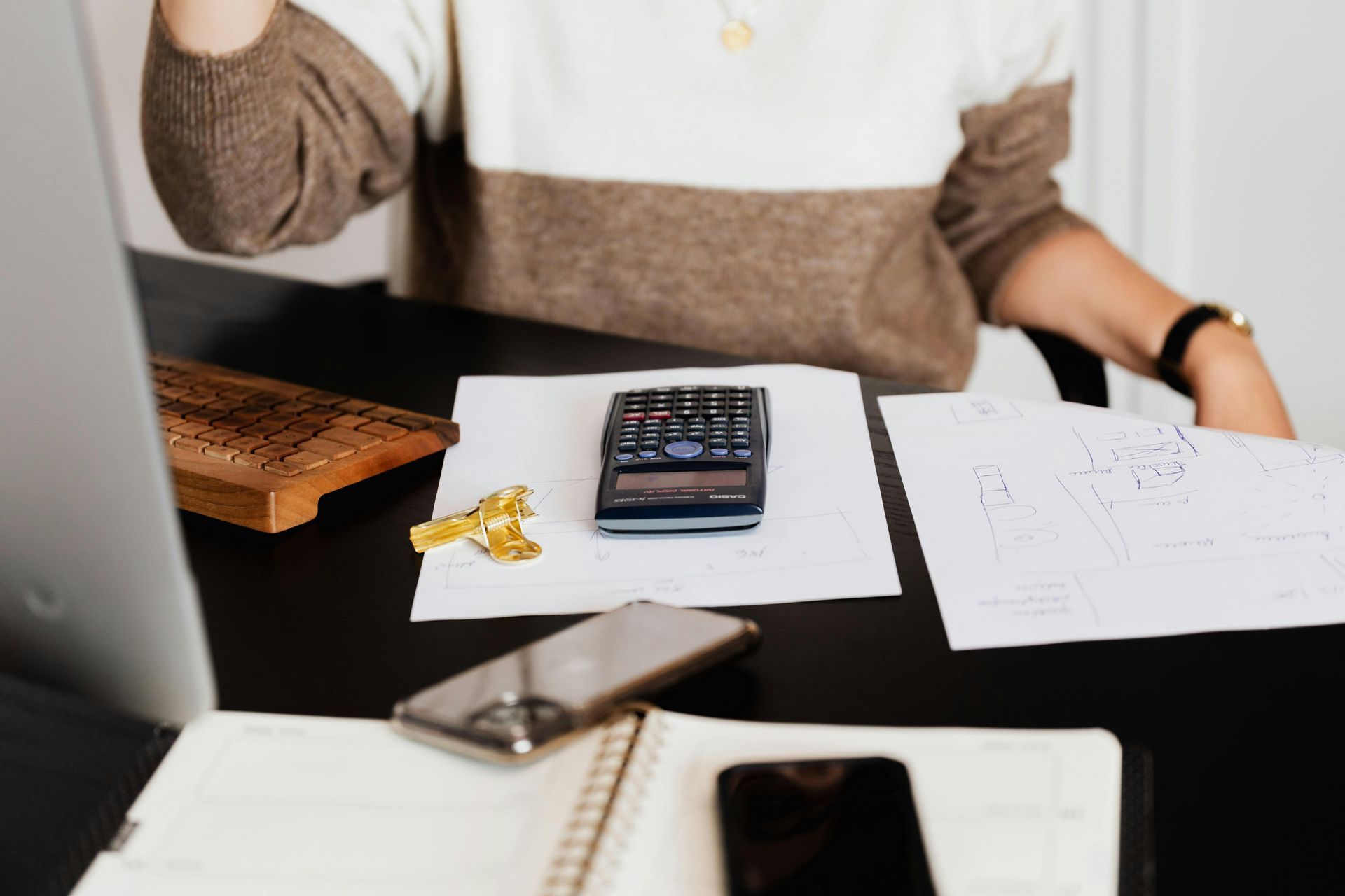 Person at desk with calculator, papers, and two smartphones.