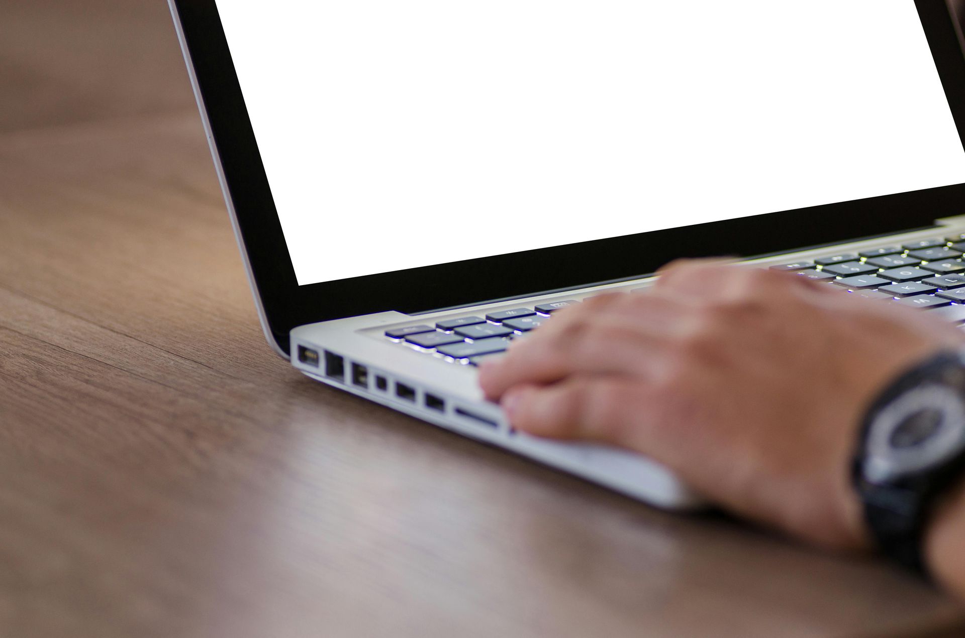 A person's hand typing on a laptop with a blank white screen, set on a wooden surface.