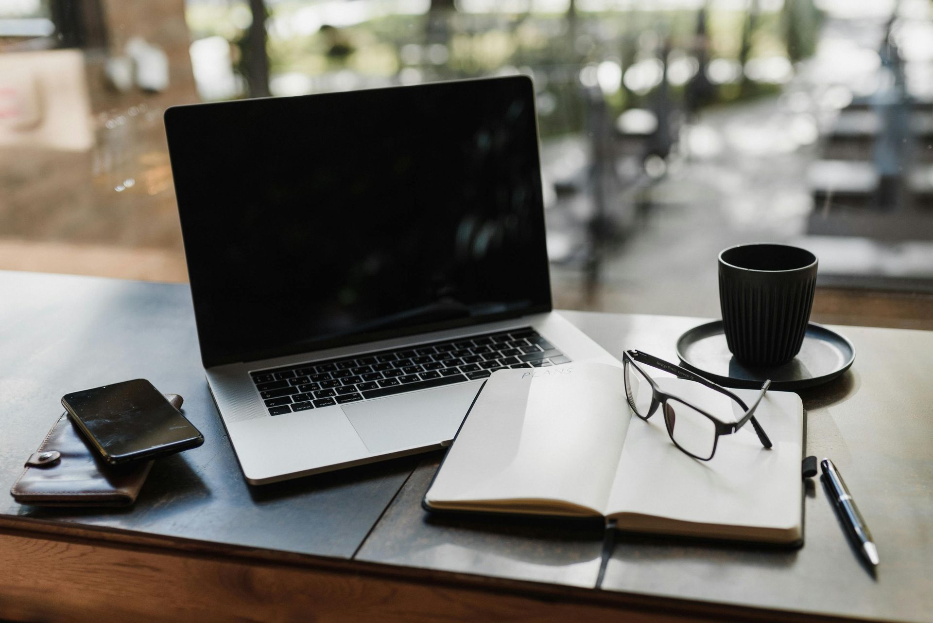 Laptop, notebook, glasses, and coffee cup on a table.