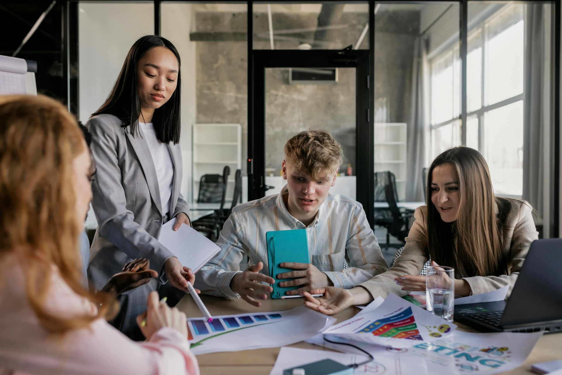 A team sits around a conference table in a modern office, collaborating on documents and charts during a meeting.