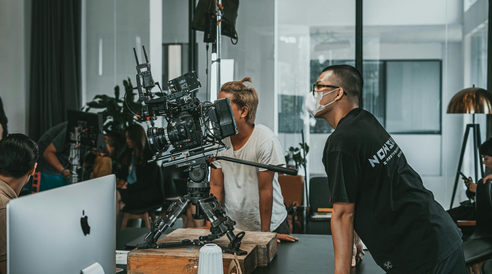 Film production crew members observing a professional camera on a tripod in a bright, modern studio space.