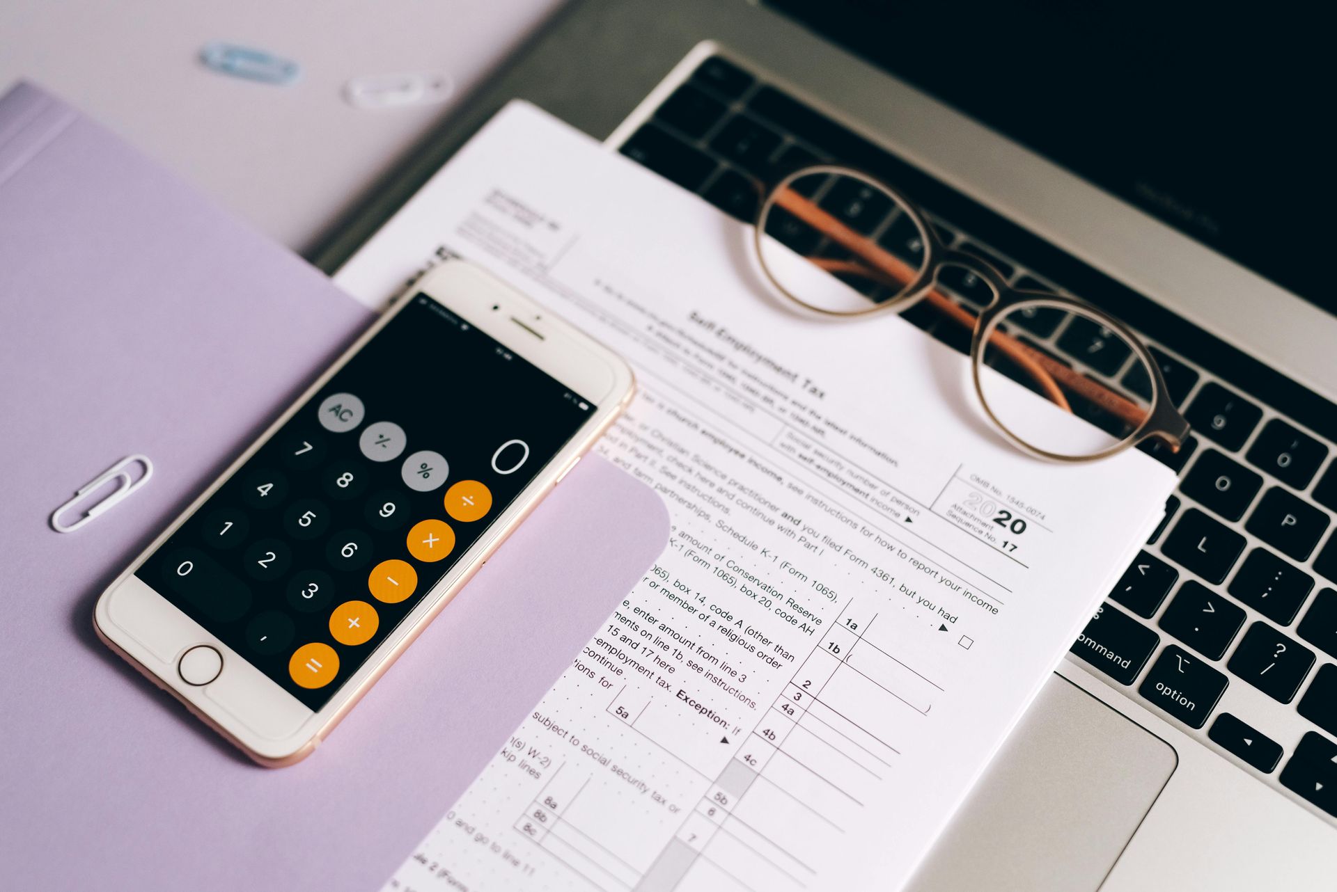 Smartphone, eyeglasses, and papers on a laptop keyboard, with a calculator and notebook nearby.