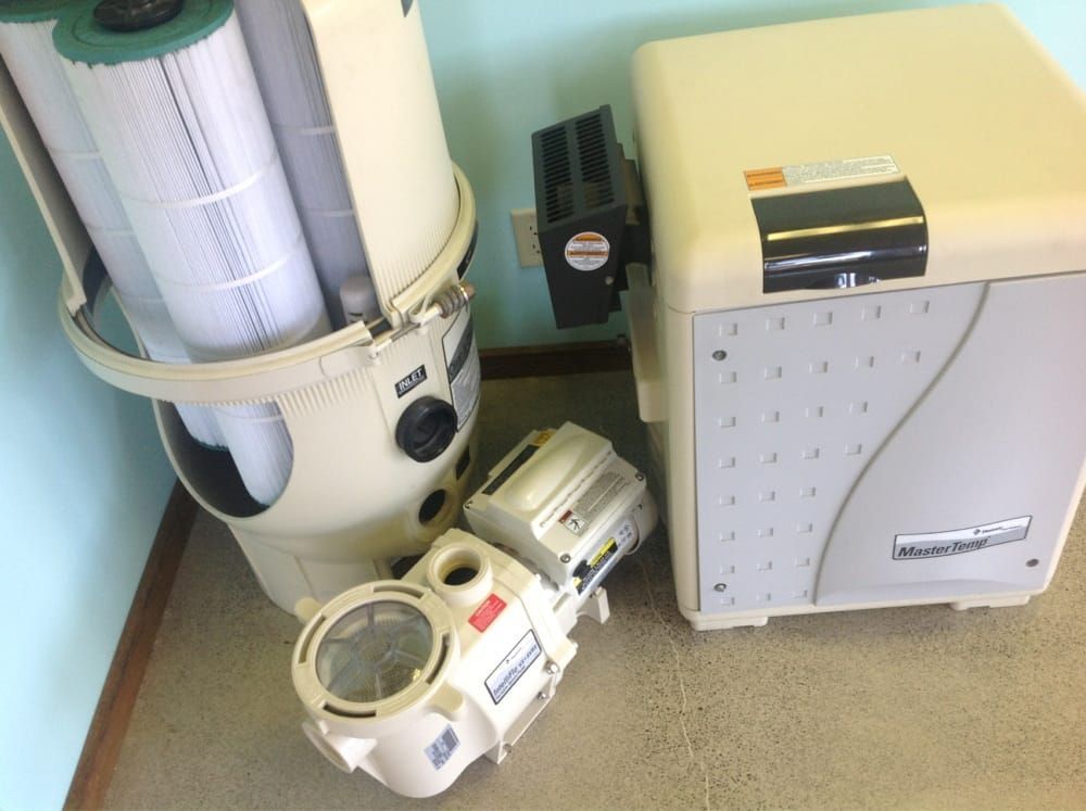 Assorted vacuum cleaner parts and machines in a corner of a room, including a white canister and beige unit.