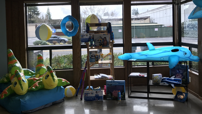 Colorful playroom with inflatable toys, shelves, and a blue shark-shaped padded mat by large windows