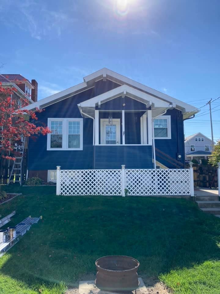 Blue house with white trim, porch, and lattice fence. Bright, sunny day.