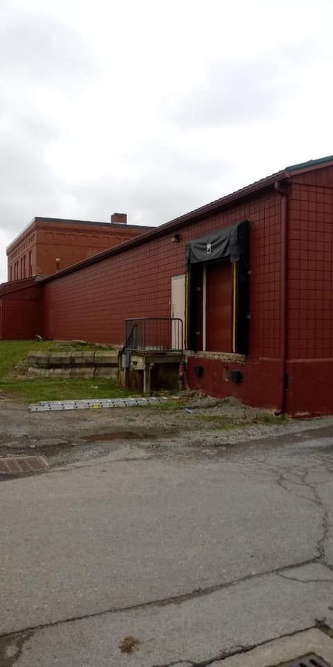 A weathered brick building with a loading dock and a cloudy sky overhead.