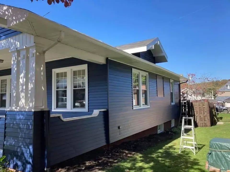 Blue house exterior with white trim and windows, a ladder, and a green lawn.