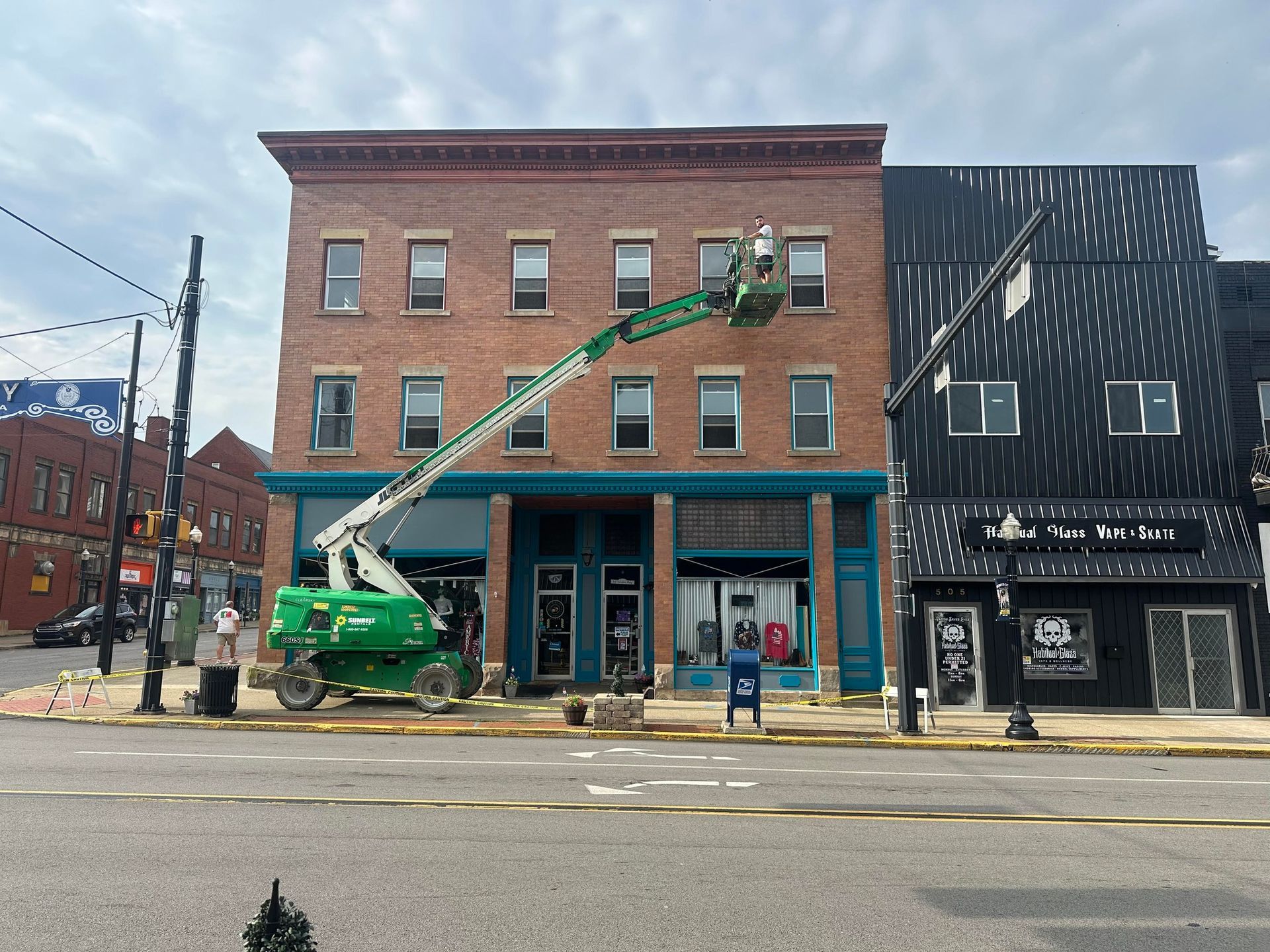 Building with a lift for construction; teal awning, brick and black exterior buildings; street view.