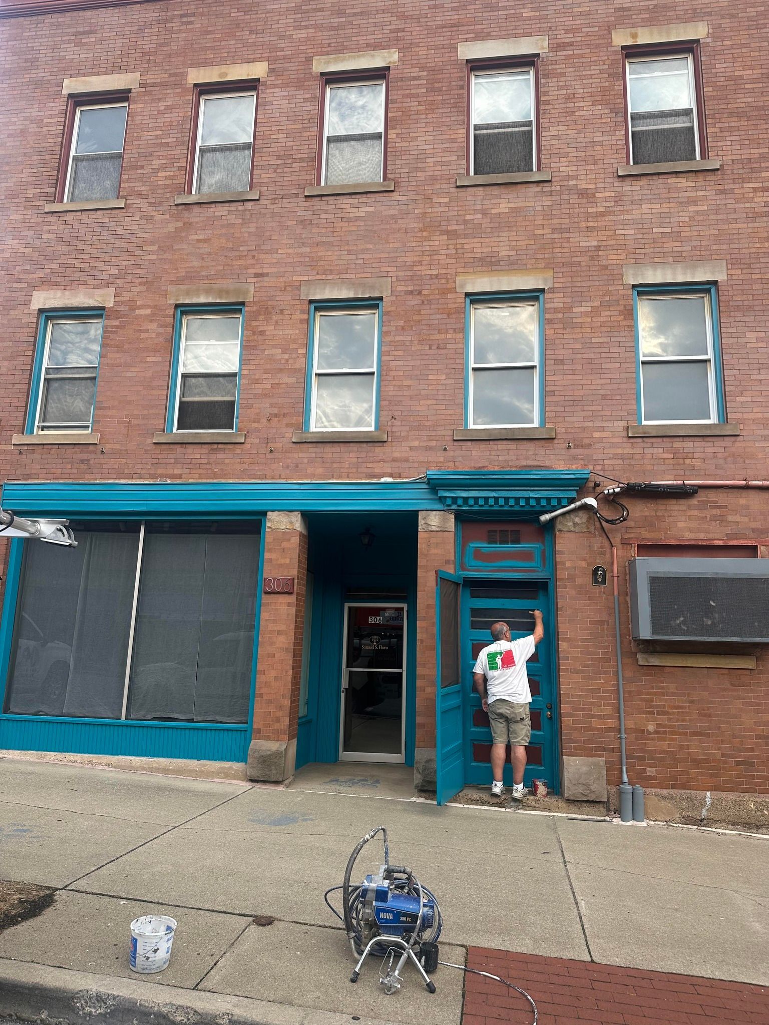 Brick building with teal trim and a man painting the entrance.