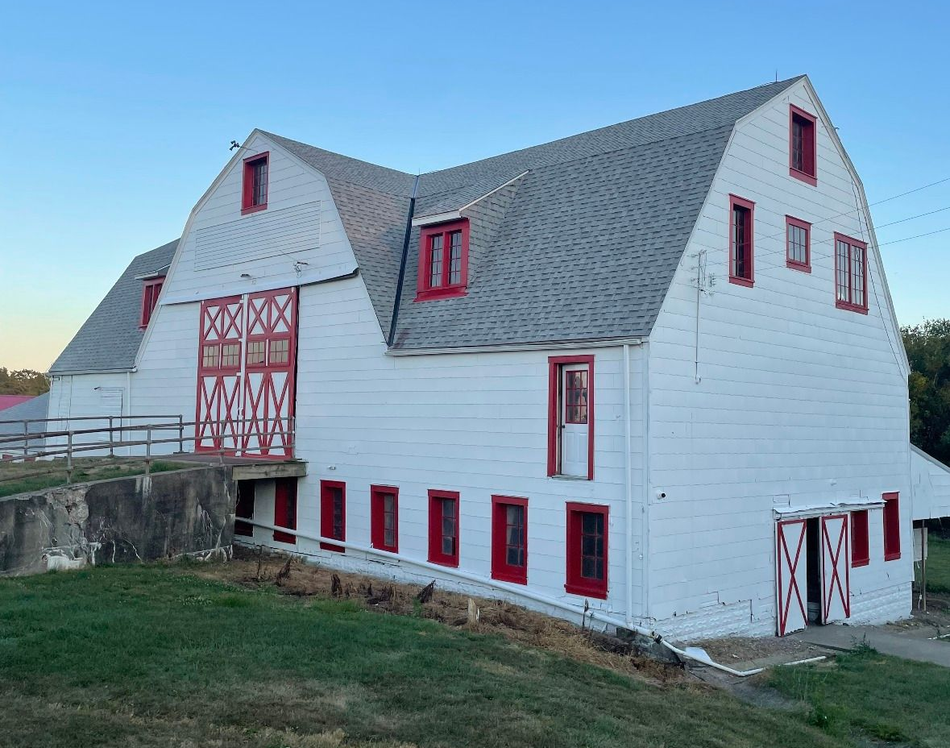 White barn with red trim against a blue sky, set on a grassy hill.
