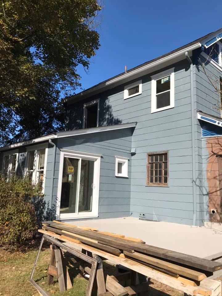 Blue-sided house with new white window frames and a sliding glass door. Construction materials are in the foreground.