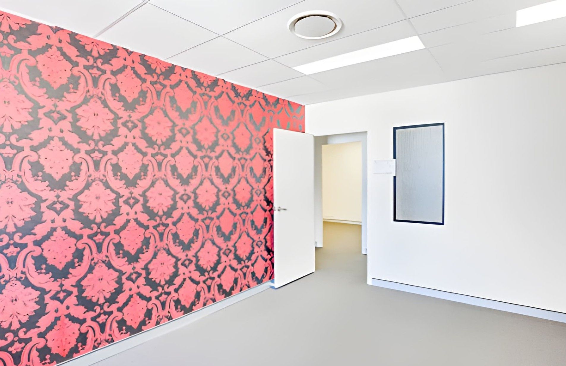 A vintage chair sits before striped wallpaper, with potted cacti and plants in an otherwise minimal interior.