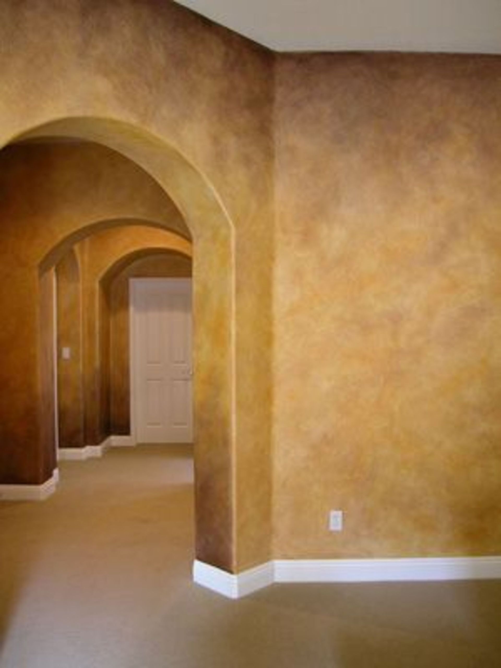 Arched doorways leading down a hallway with textured brown and tan walls and white baseboards.