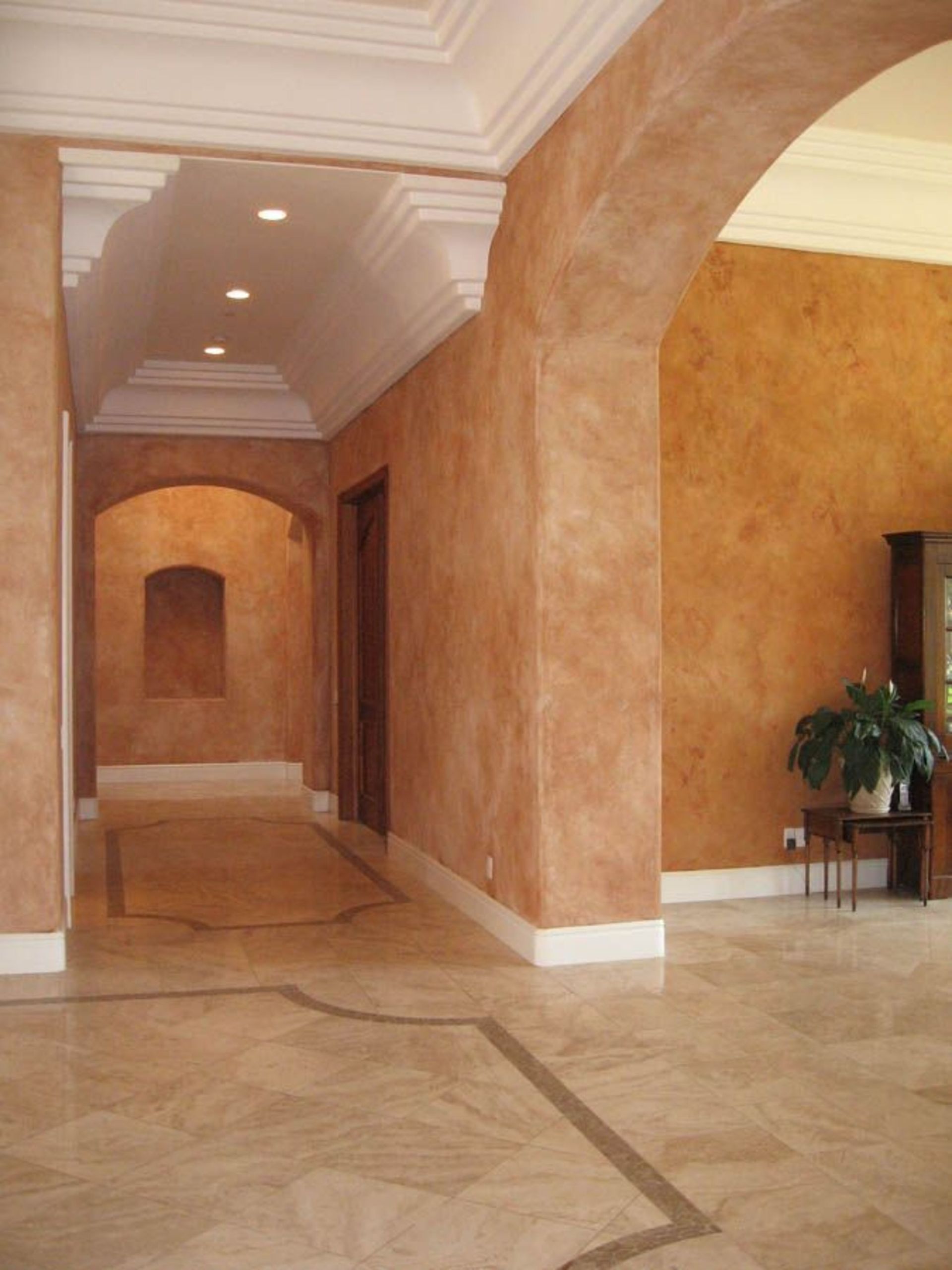 Interior view of a hallway with orange textured walls, marble floor, and arched doorways.