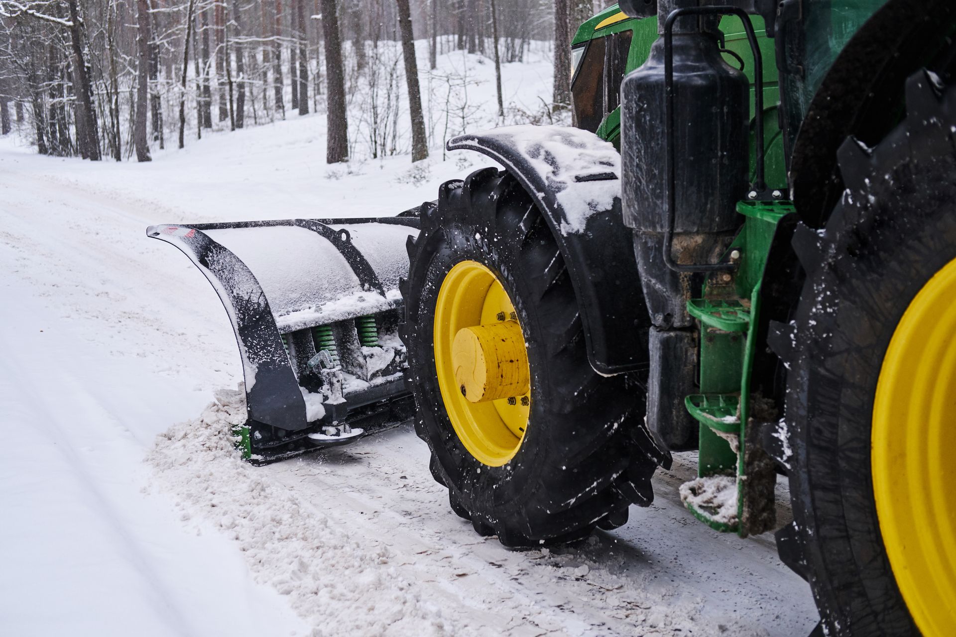 A green and yellow tractor is plowing snow on a snowy road.