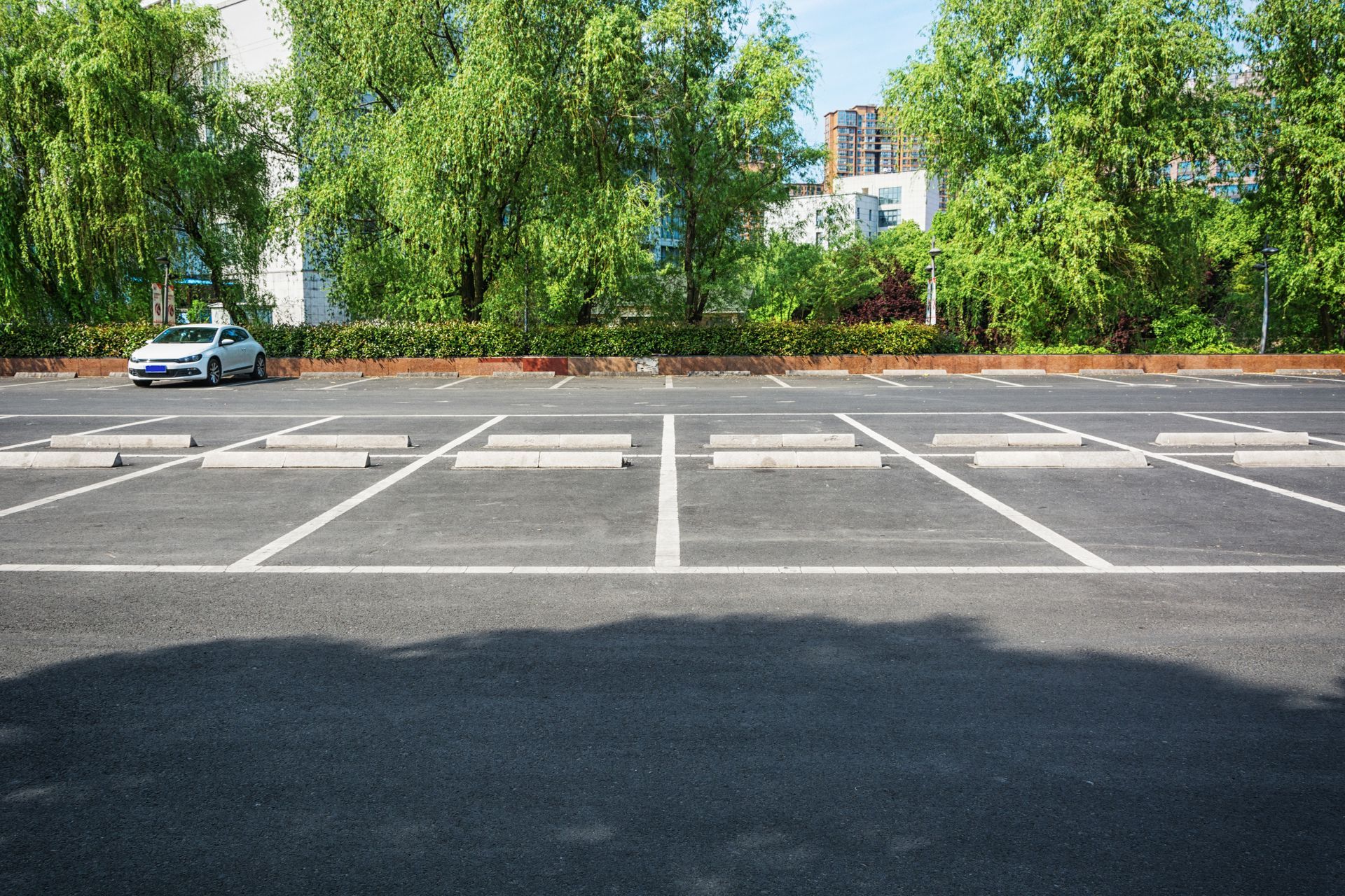 A car is parked in an empty parking lot with trees in the background.