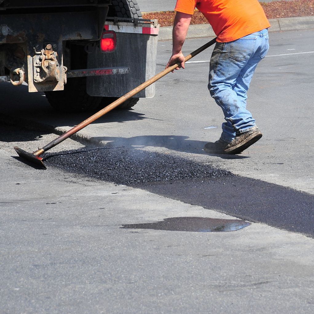 A man is using a broom to spread asphalt on the road